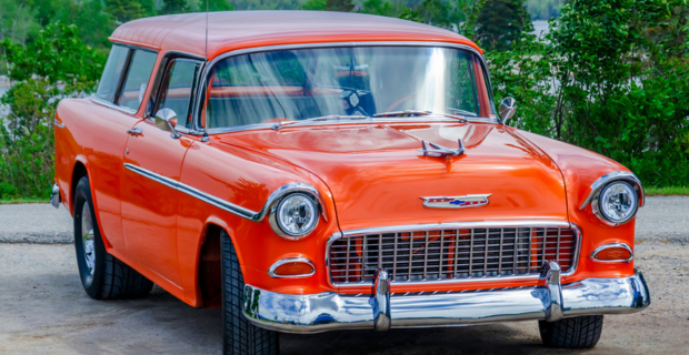 Une Chevy Nomad 1955 orange stationnée devant une forêt verte