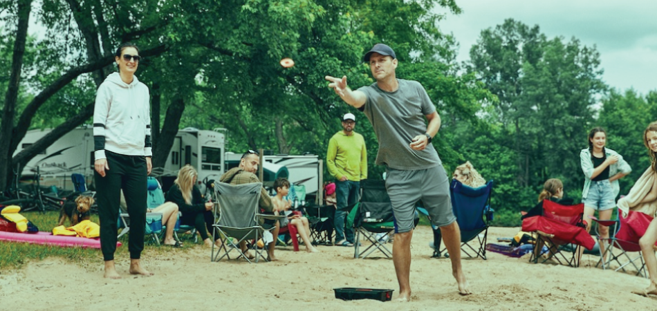 Homme jouant au jeu de washers sur un terrain de camping.
