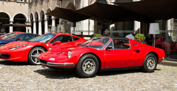 De magnifiques Ferrari rouges et une superbe Ferrari bleue sont garées sur une route pavée devant un bâtiment en miroir avec des arches et des parasols extérieurs.