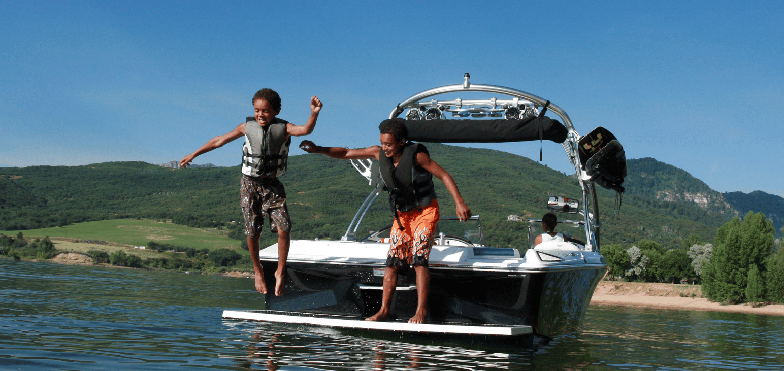 Deux jeunes garçons sautant d’un bateau de wakeboard sur un lac, équipés de gilets de sauvetage.  
