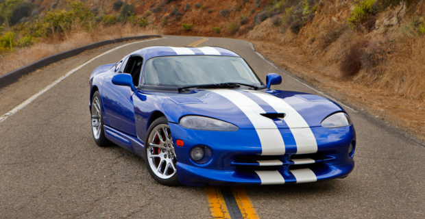 Une Dodge Viper GTS bleue avec des bandes décoratives est stationnée au milieu d'une route dans des collines.