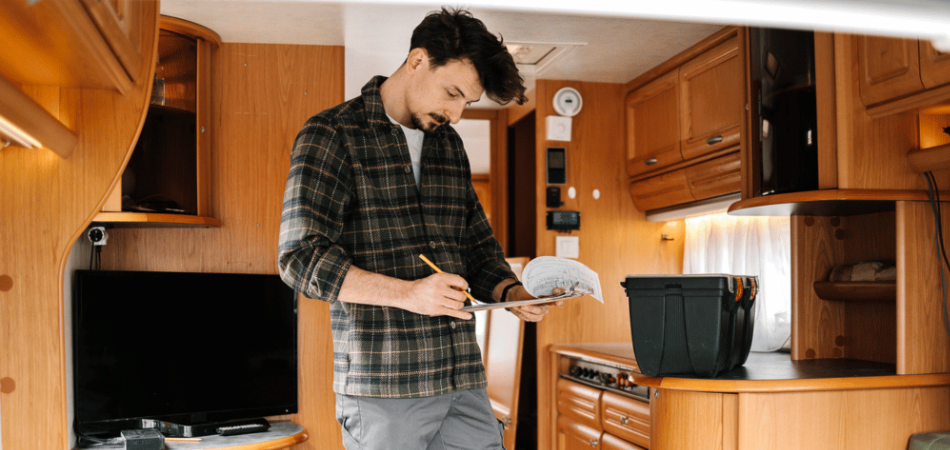 Un homme debout dans son véhicule récréatif avec un bloc-notes, en train de parcourir sa liste de contrôle pour l’entretien printanier de son véhicule récréatif en vue de la saison à venir.