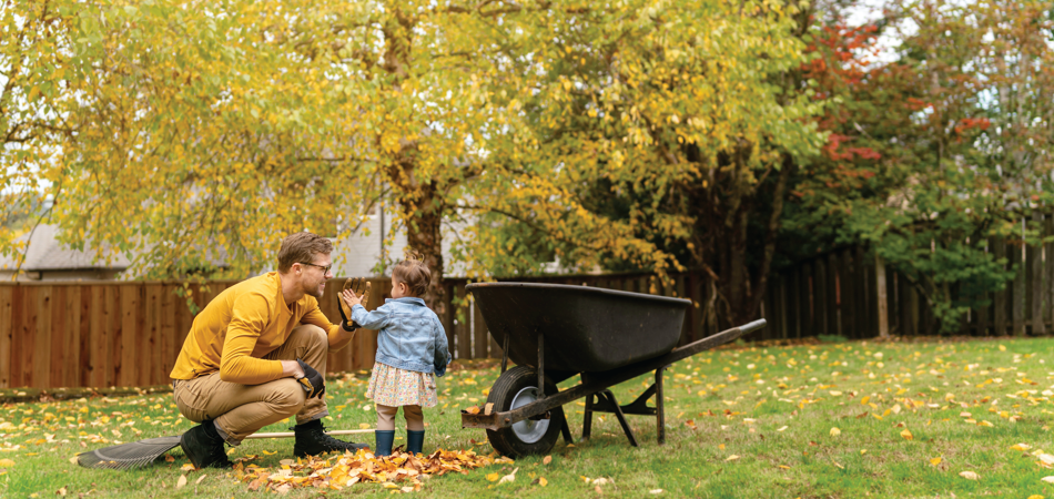 Une personne et un enfant dans une cour avec des feuilles d'automne à côté d'une brouette.