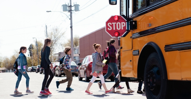 Les élèves traversent en toute sécurité devant un autobus scolaire. Le panneau d’arrêt de l’autobus est déployé et ses feux clignotent.