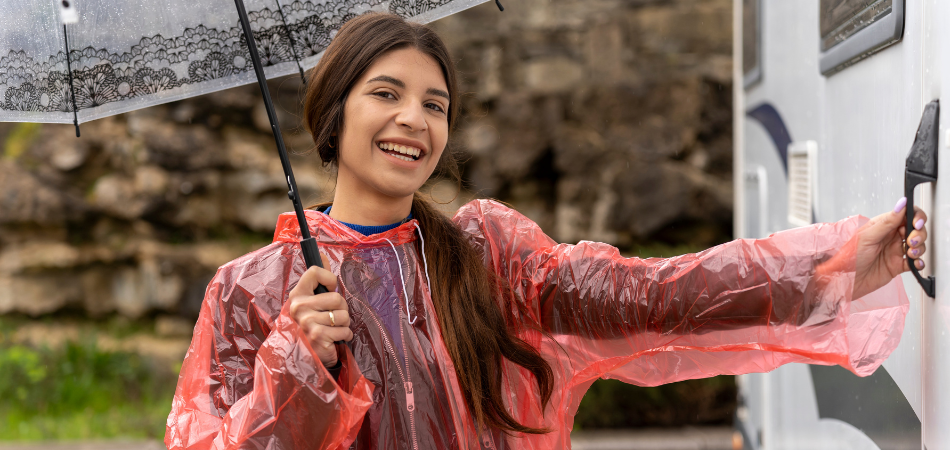 Une femme souriante, munie d’un parapluie et d’un poncho de pluie, s’apprêtant à ouvrir la porte de son VR.
