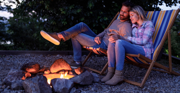 Un homme et une femme assis au bord d’un feu de camp se tiennent la main durant une soirée calme. 