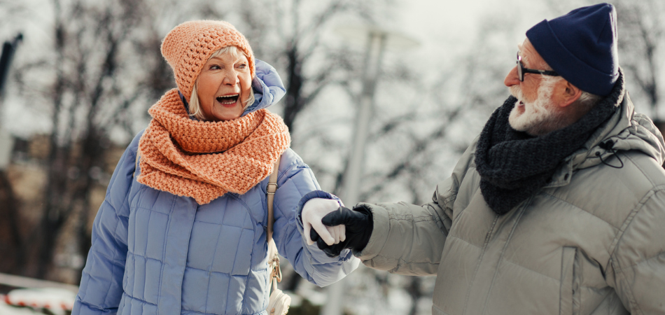 Deux personnes vêtues de manteaux d’hiver épais, d’écharpes et de gants marchant main dans la main sur un chemin enneigé, illustrant un guide de sécurité hivernale.
