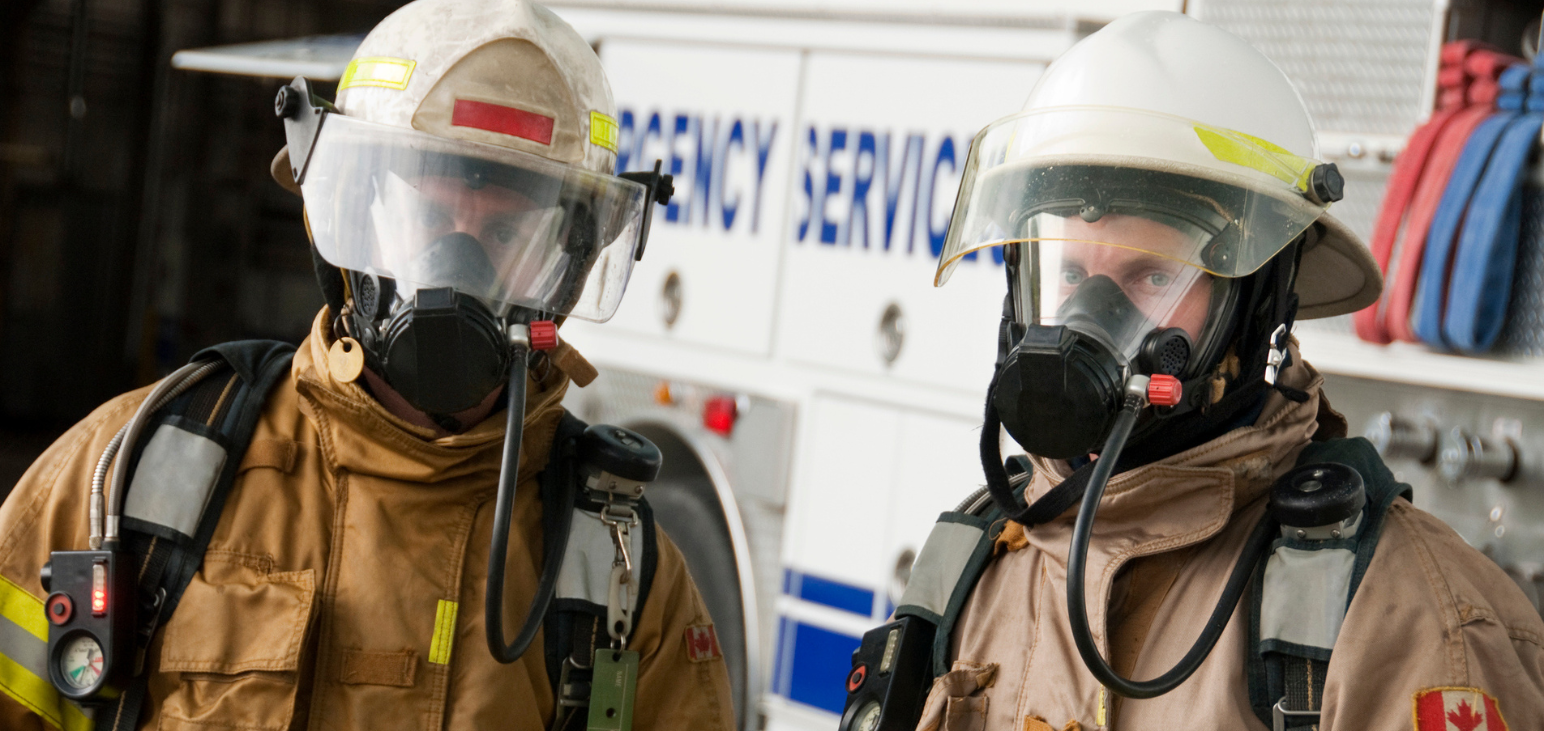 Deux pompiers canadiens en tenue d’intervention devant leur camion de pompiers discutent d’Intelli-feu et donnent leurs meilleurs conseils pour prévenir les incendies.