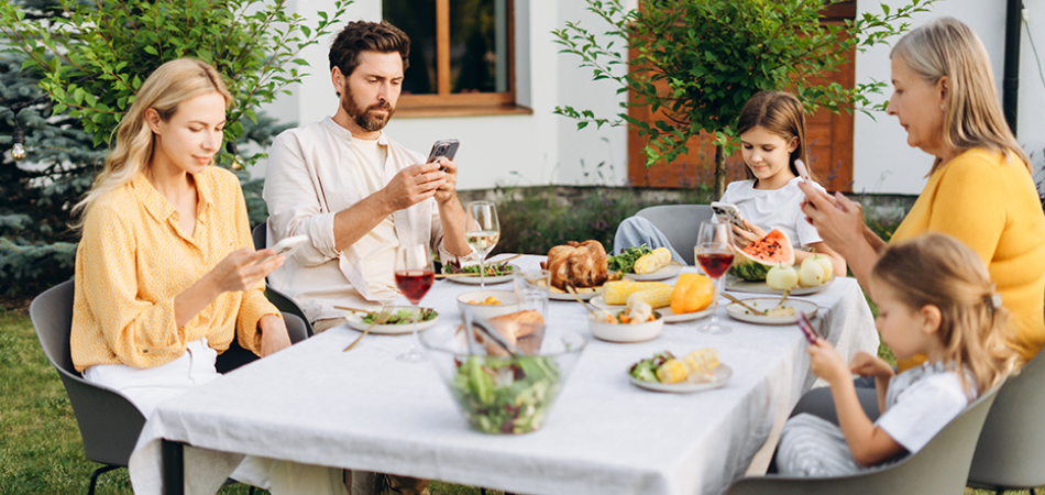 Une famille réunie autour de la table pour le repas, mais dont les membres sont absorbés par leurs écrans.