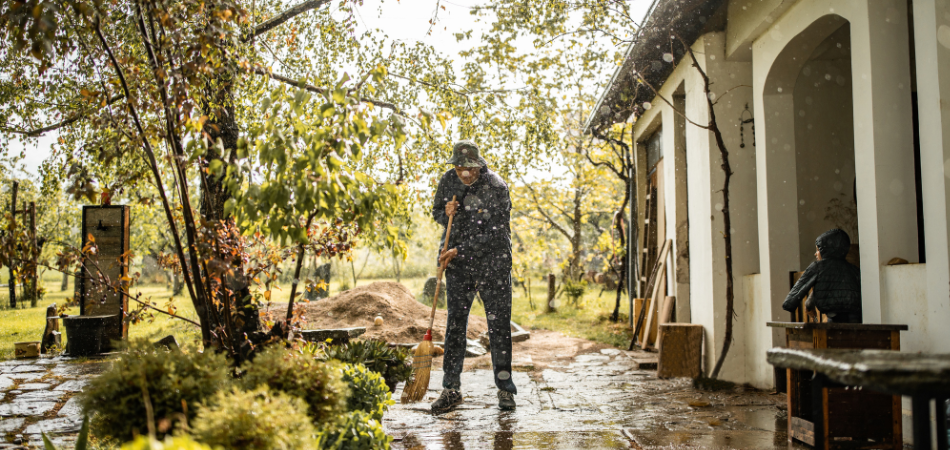 Un propriétaire dans sa cour arrière inondée, en train de balayer l'eau loin de sa maison par un jour de pluie.