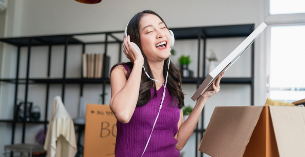 Une jeune femme écoute de la musique pendant qu’elle déballe des boîtes dans son logement loué. 