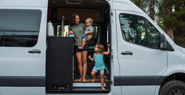 Une femme debout dans son autocaravane tenant un enfant et lui préparant à manger.