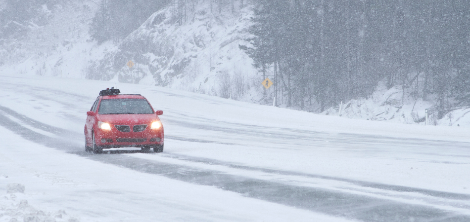 un véhicule rouge roulant sur une route enneigée, respectant les règles de sécurité routière en hiver.
