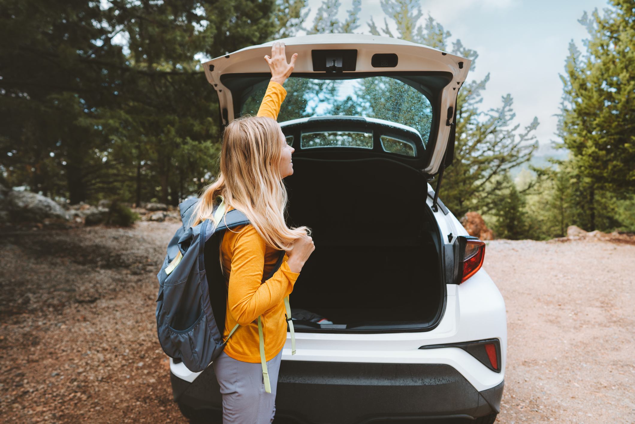 Une femme portant un sac à dos tend la main pour fermer le coffre de sa voiture