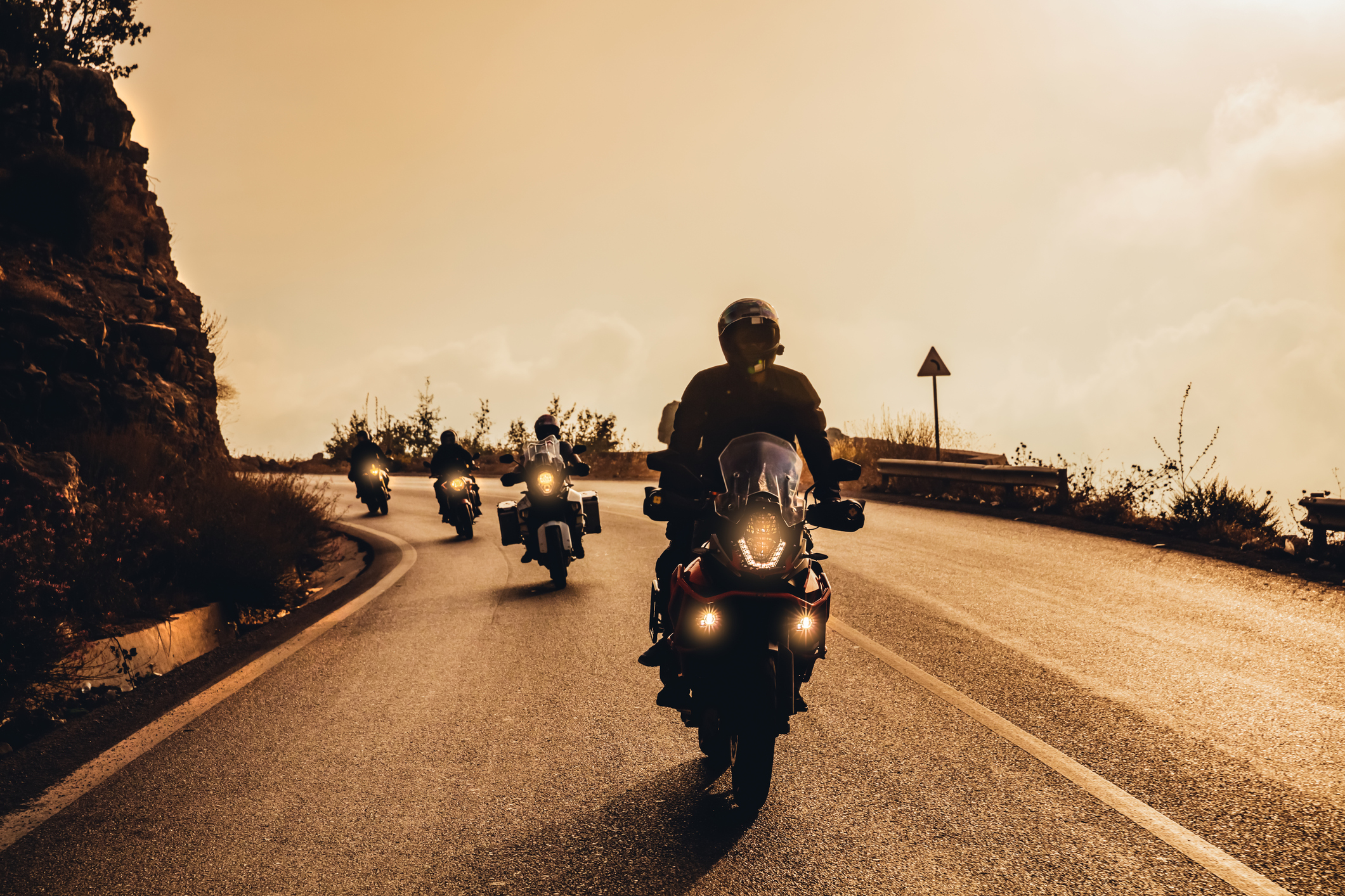 Une photo sépia de quatre motocyclistes qui se suivent de manière sécuritaire, un après l’autre, dans une courbe.