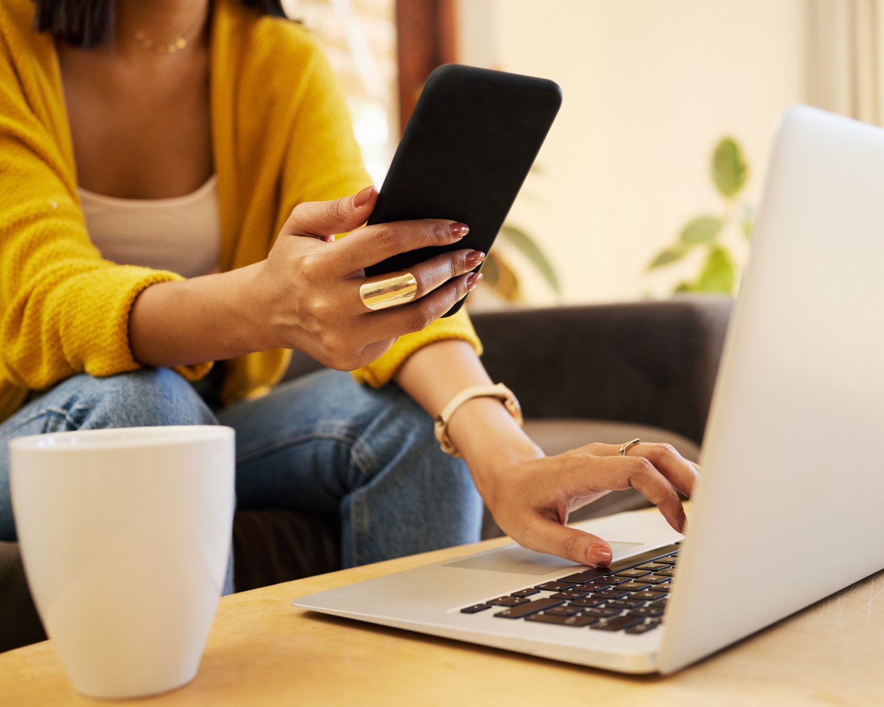 A closeup of a woman holding her phone and sitting an front of an open laptop