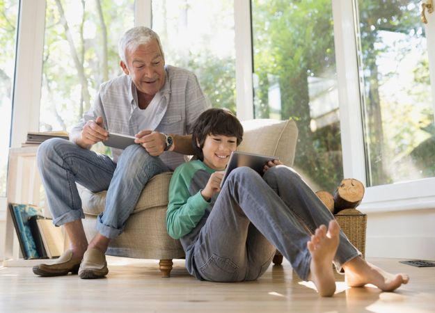  Un Canadien d'origine asiatique assis dans un fauteuil regarde son petit-fils jouer sur une tablette.