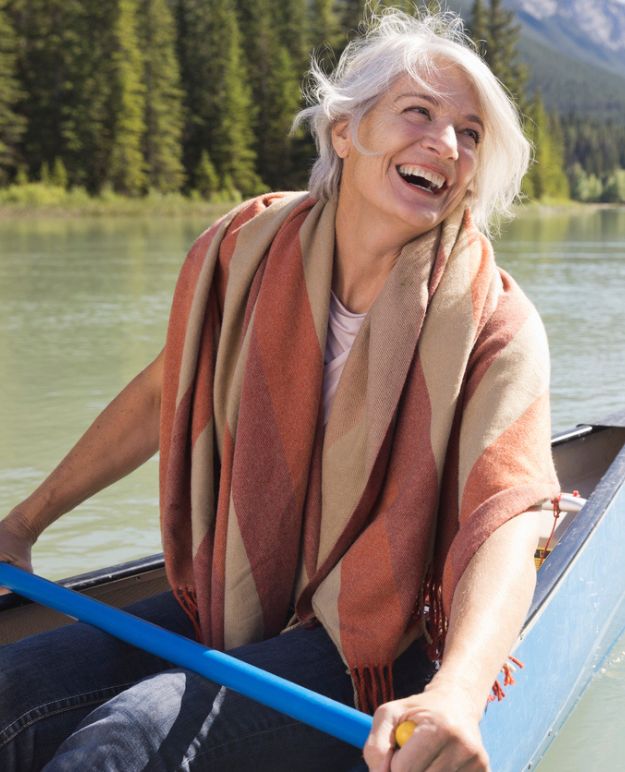 Une femme souriante aux cheveux courts en ruban pagayant son kayak lors d'une journée d'été ensoleillée en Alberta.