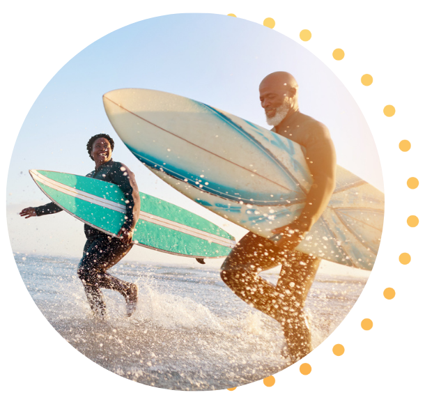 Un couple noir au début de la cinquantaine courant dans les vagues, portant des planches de surf sous le bras.