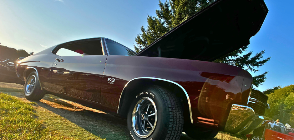 Une Chevrolet Chevelle SS rouge foncé classique, une voiture de sport puissante, garée sur l’herbe lors d’un salon automobile en plein air, photographiée sous un angle bas.