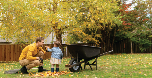 Une personne et un enfant dans une cour avec des feuilles d'automne à côté d'une brouette.