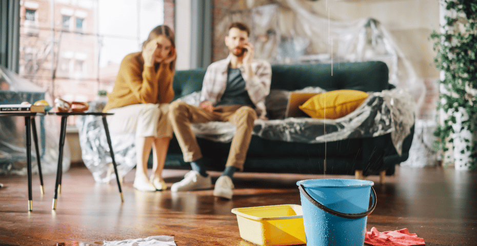 Dégâts d’eau dans un salon, avec des seaux sur le sol et des meubles recouverts de plastique pour retenir les fuites.