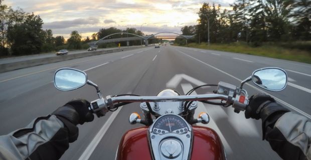 Une personne à moto roule sur l'autoroute par temps partiellement nuageux. La photo est prise du point de vue du conducteur.