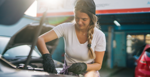 Un jeune femme regardant sous le capot d’un véhicule afin d’effectuer l’entretien printanier de sa voiture classique et de la préparer à prendre la route.
