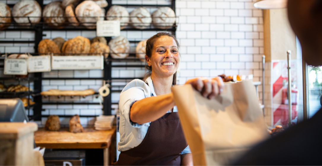 Propriétaire d’entreprise heureuse dans sa boulangerie remettant un emballage à emporter à un client.