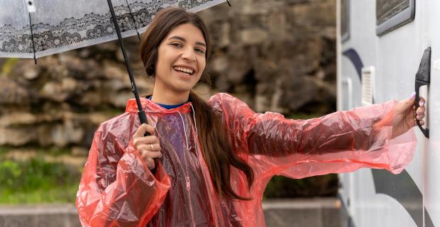 Une femme souriante, munie d’un parapluie et d’un poncho de pluie, s’apprêtant à ouvrir la porte de son VR.