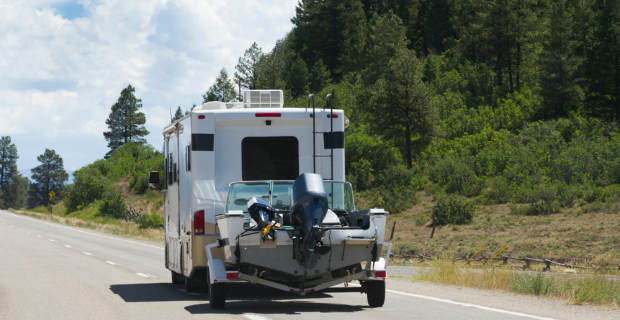 Une autocaravane remorque un bateau sur une route dégagée en été.