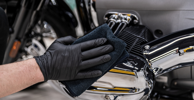 Une main gantée nettoie le moteur d’une moto lors des préparatifs pour le remisage hivernal.  