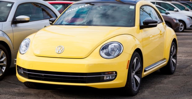 Profil avant et latéral d’une Volkswagen Beetle jaune garée chez un concessionnaire. 