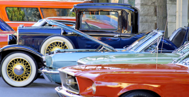 Un ensemble de magnifiques voitures anciennes, de collection et classiques est fièrement exposé sous le soleil d’été. Les superbes voitures orange, bleues et vertes sont exposées avec le capot relevé ou abaissé.