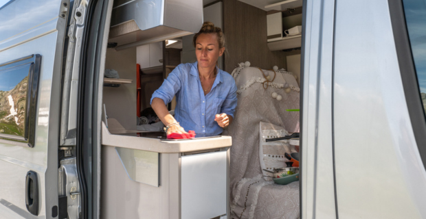 Une femme nettoie la cuisinière dans son autocaravane avec la porte ouverte.