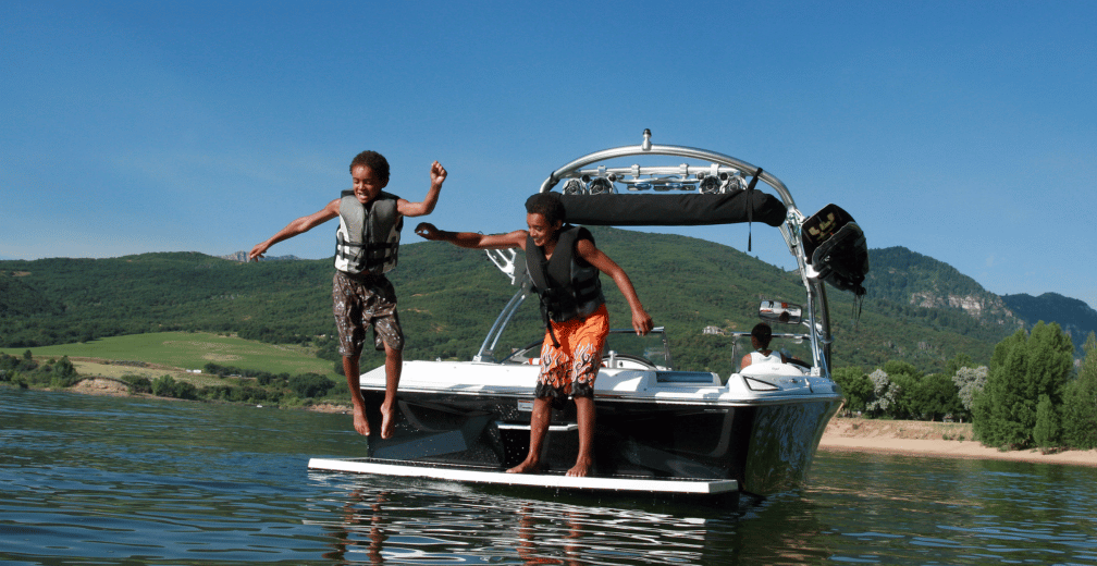 Deux jeunes garçons sautant d’un bateau de wakeboard sur un lac, équipés de gilets de sauvetage.