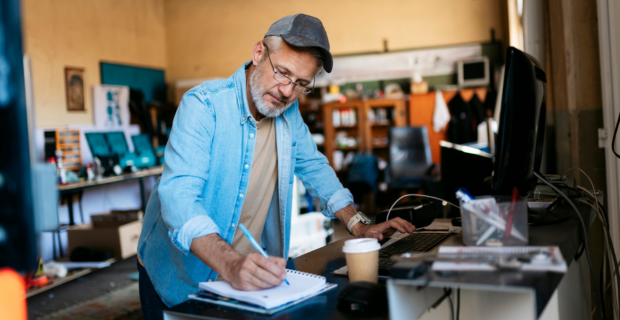 Un homme d’âge mûr est dans son atelier, en train de prendre des notes et de planifier les tendances en matière d’assurance des entreprises pour 2026.  