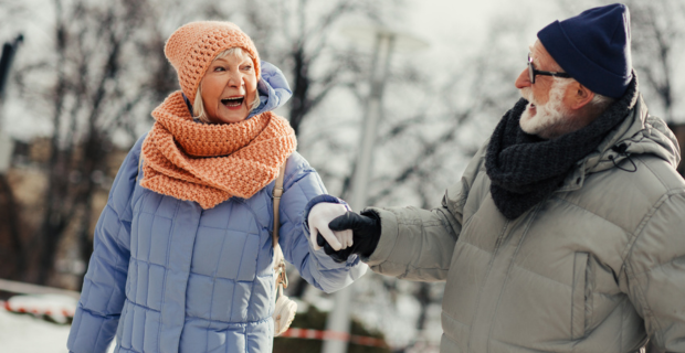 Deux personnes vêtues de manteaux d’hiver épais, d’écharpes et de gants marchant main dans la main sur un chemin enneigé, illustrant un guide de sécurité hivernale.