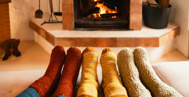 Trois paires de pieds qui portent toutes des bas aux couleurs différentes devant un foyer pour se garder au chaud pendant l’hiver. 